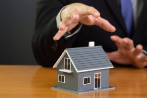 Uomo in giacca e cravatta che fa il gesto di afferrare una casa in miniatura