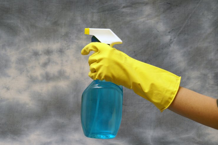 Persona con un guanto e un flacone spray per le pulizie