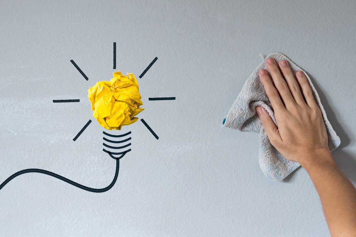 Mano che passa uno straccio sul muro e simbolo di una lampadina (idea)