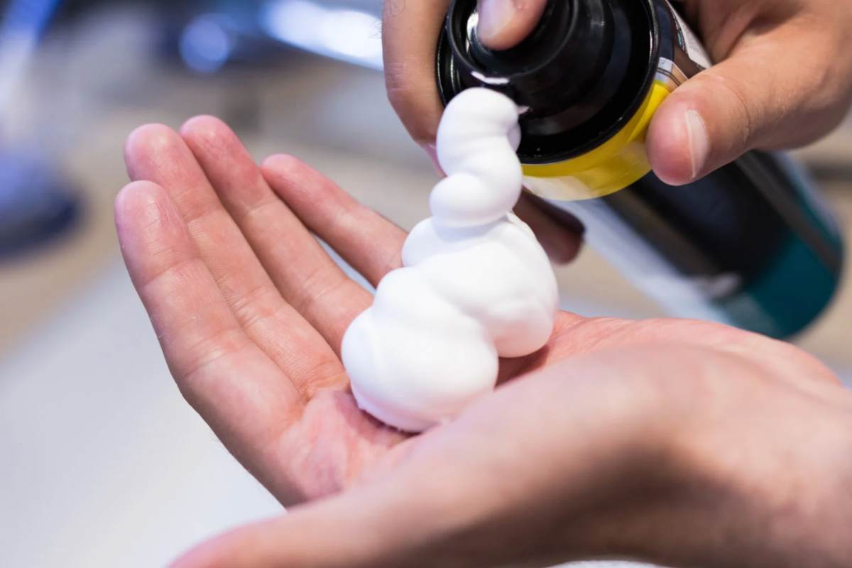 Persona che spruzza schiuma da barba sulla mano