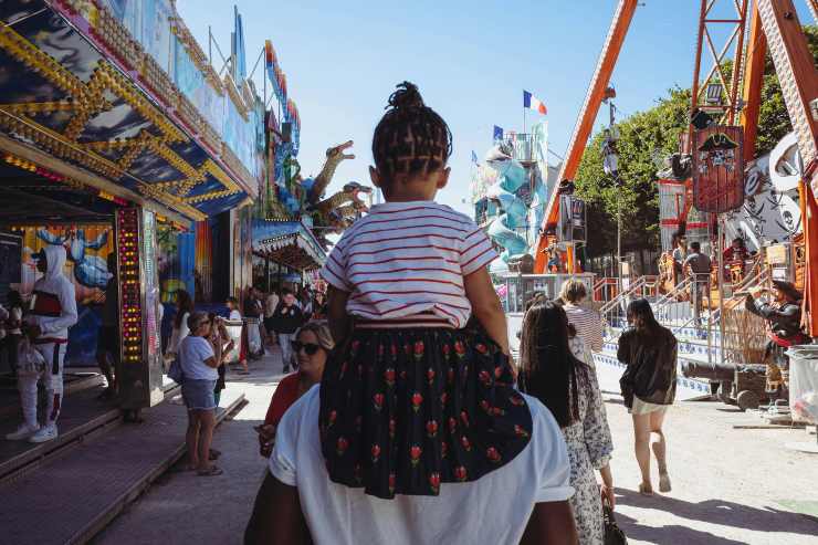 Bambina sulle spalle del padre in un parco divertimenti