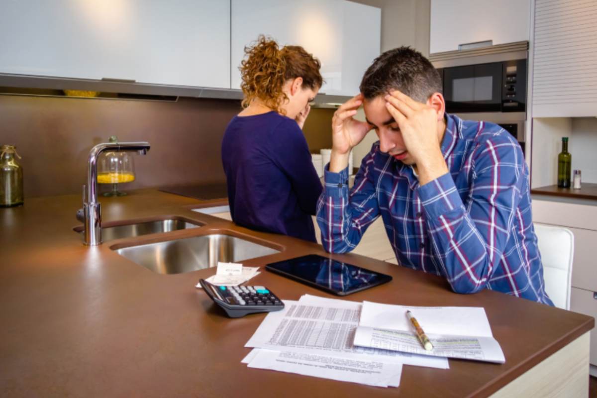 uomo e donna disperati in cucina che fanno i calcoli con calcolatrice e fogli