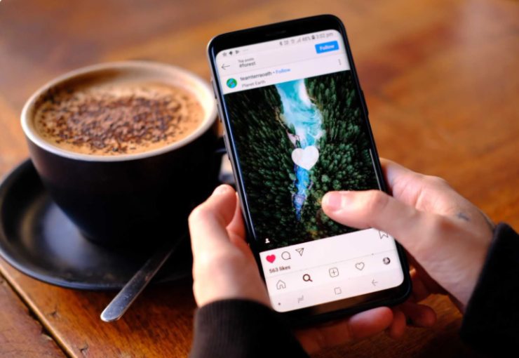 persona con in mano lo smartphone e davanti un cappuccino